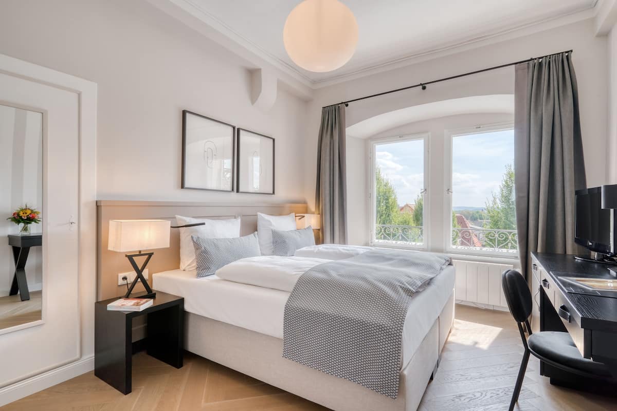 A modern bedroom with a bed, bedside table, lamp, and a TV.