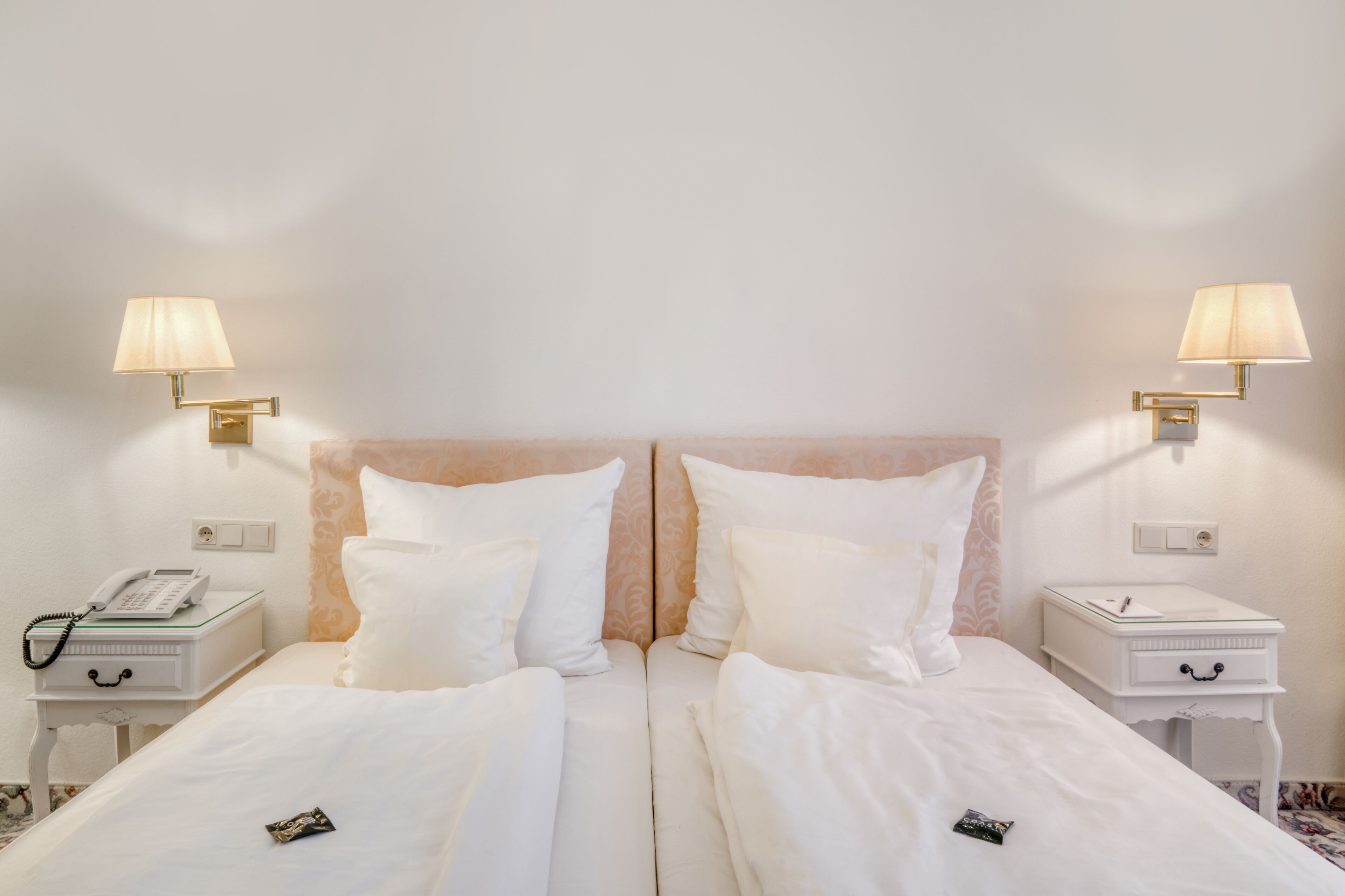 A hotel room with two beds, a bedside telephone, and two bedside lamps.