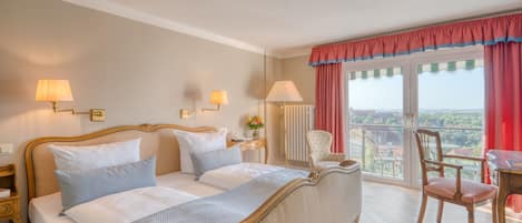 Habitación de hotel con una cama grande, dos mesitas de noche, una silla, una pequeña mesa y vistas a la ciudad.
