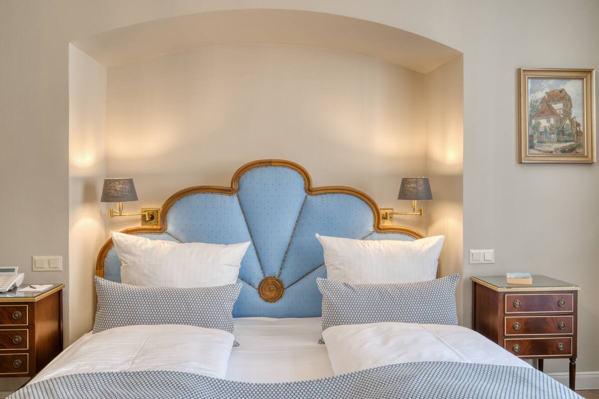 A hotel room with a large bed, two bedside tables, a nightstand, a wall-mounted lamp, and a framed picture.