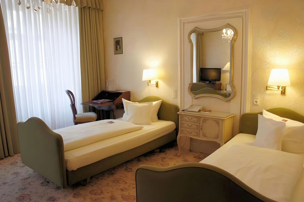 A hotel room with two single beds, a desk, a chair, a dresser, and a mirror.