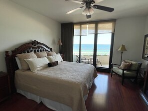 A large bed with a wooden headboard, a ceiling fan, and a view of the ocean through a sliding door.