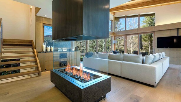 A modern living room with a glass-top fire feature, a white sofa, and a wooden staircase. - Modern Vail Winter Escape by InvitedHome | Walk to Ski Shuttle, Hot Tub (Vail)