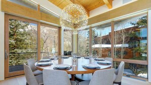 A modern dining room with a large round table, grey upholstered chairs, and a unique spherical chandelier. - Modern Vail Winter Escape by InvitedHome | Walk to Ski Shuttle, Hot Tub (Vail)
