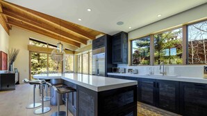 A modern kitchen with a large island, bar stools, and a view of the outdoors through large windows. - Modern Vail Winter Escape by InvitedHome | Walk to Ski Shuttle, Hot Tub (Vail)