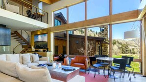 A spacious living area with a large sofa, a dining table with chairs, and a staircase leading to an upper level. - Modern Vail Winter Escape by InvitedHome | Walk to Ski Shuttle, Hot Tub (Vail)