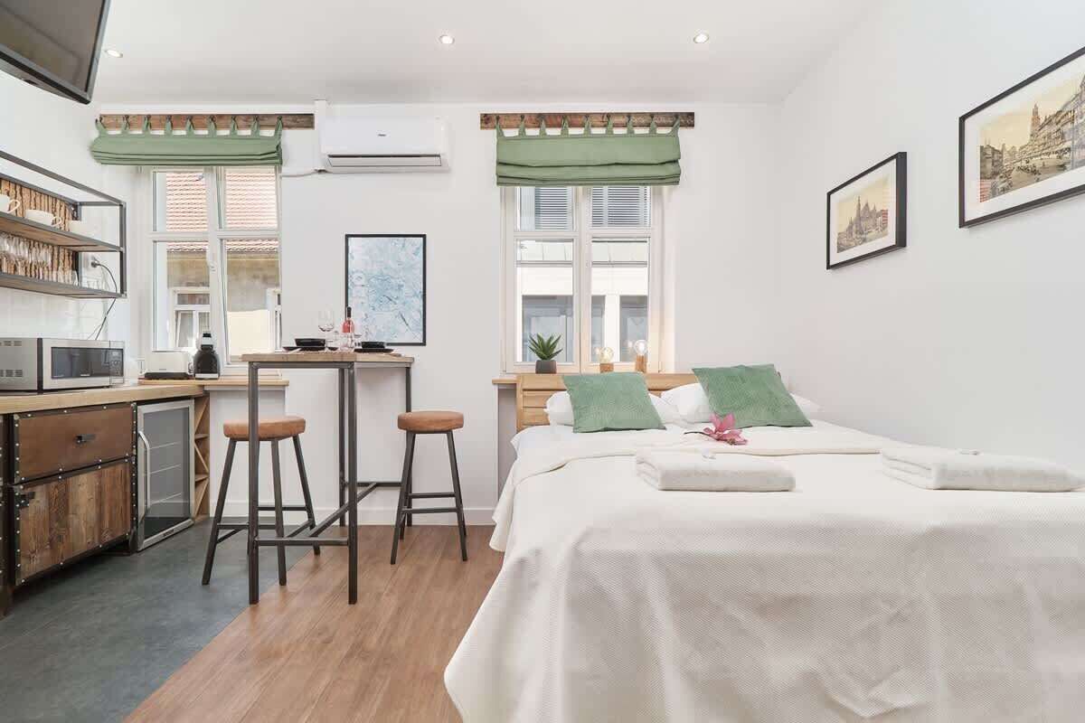 Une chambre moderne avec un lit, un bureau et une chaise. Une fenêtre offre une vue sur les bâtiments à l’extérieur.