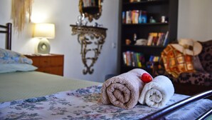 Een net opgemaakt bed met bloemenbeddels, een bedlampje, een boekenplank en een decoratieve spiegel.