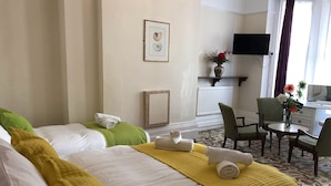 Habitación de hotel con dos camas, un escritorio con una silla, un televisor y un florero con flores.