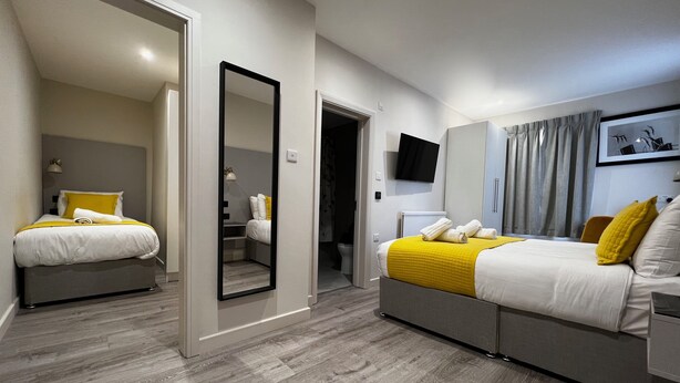 Una habitación de hotel moderna con dos camas, un espejo grande, un televisor de pantalla plana y un armario.