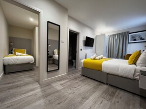 A modern hotel room with two beds, a large mirror, a flat-screen TV, and a wardrobe. - Pearl & Pebbles Eastbourne (Eastbourne)