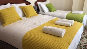Habitación de hotel con dos camas, cada una con ropa blanca y colchas amarillas. Hay toallas sobre las camas y una manta verde sobre una de ellas.