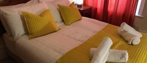 A neatly made bed with white and yellow bedding, a wooden headboard, and a bedside table with a lamp.