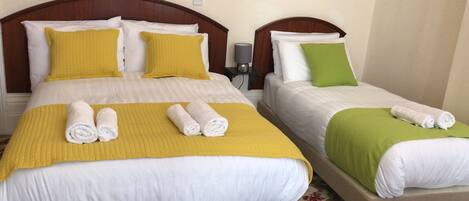Two twin beds with yellow and green bedding, white pillows, and rolled towels.