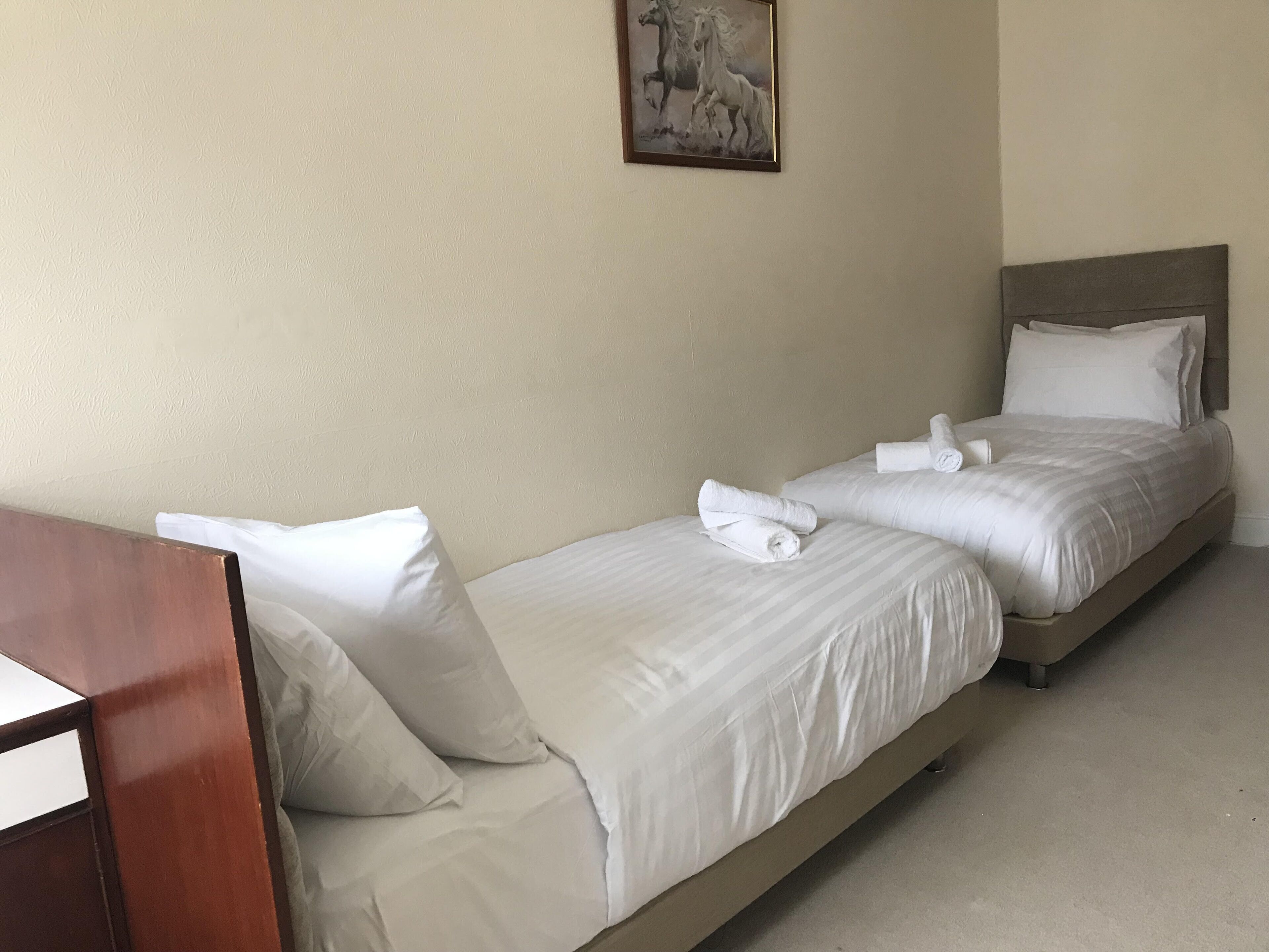 Habitación de hotel con dos camas, cada una con sábanas y almohadas blancas, cabeceros de madera y un cuadro de caballos en la pared.