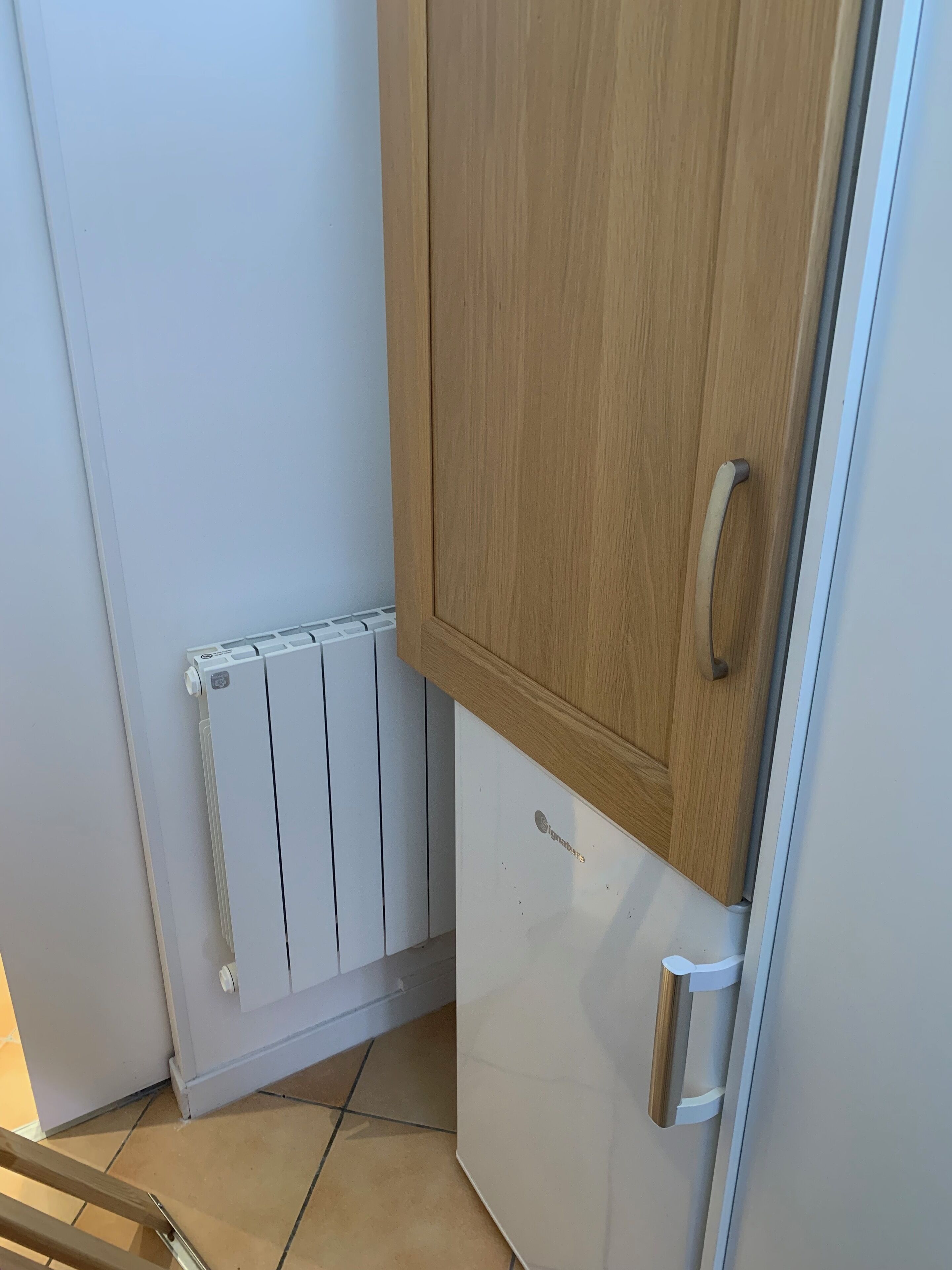 A corner of a room with a white radiator, a wooden cabinet, and a white door with a silver handle.