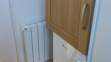 A corner of a room with a white radiator, a wooden cabinet, and a white door with a silver handle.