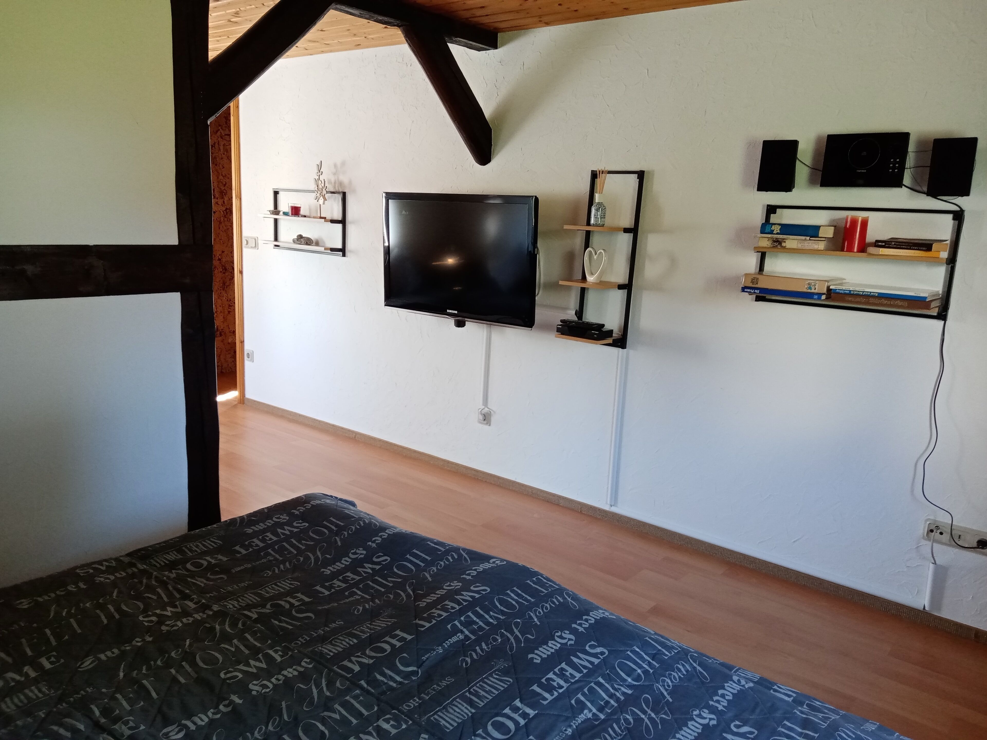 Une chambre comprenant un lit, un téléviseur à écran plat fixé au mur et une étagère avec des livres et des objets de décoration.