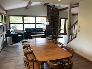 Un salón comedor amplio con una gran mesa de madera, asientos cómodos, una chimenea y ventanas grandes que ofrecen vistas al exterior.