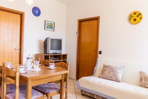 Un cuarto acogedor con una mesa de madera dispuesta para cuatro comensales, un sofá, un televisor en un estante y un reloj en la pared.