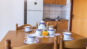 A dining table set with white and blue tea sets, a yellow rose, and wooden chairs in a room with wooden cabinets and a white refrigerator. - Holiday Apartment of Your Dreams a2a (Pag)