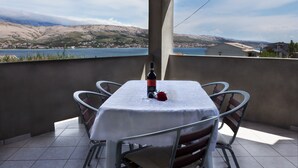 A table set for two with a bottle of wine and a rose on a balcony overlooking a lake and hills. - Holiday Apartment of Your Dreams a2a (Pag)