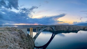 A bridge over a calm body of water with a rocky shoreline. - Holiday Apartment of Your Dreams a2a (Pag)