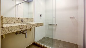 Une salle de bain avec un lavabo surmonté d’un plan de travail en granit, une douche à parois de verre et un sol carrelé de couleur blanche.