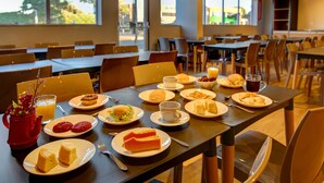 Un coin repas avec des tables préparées pour le petit-déjeuner, comprenant des assiettes remplies de nourriture, des tasses et une théière rouge.