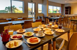 A dining area with tables set for breakfast, including plates of food, cups, and a red teapot.