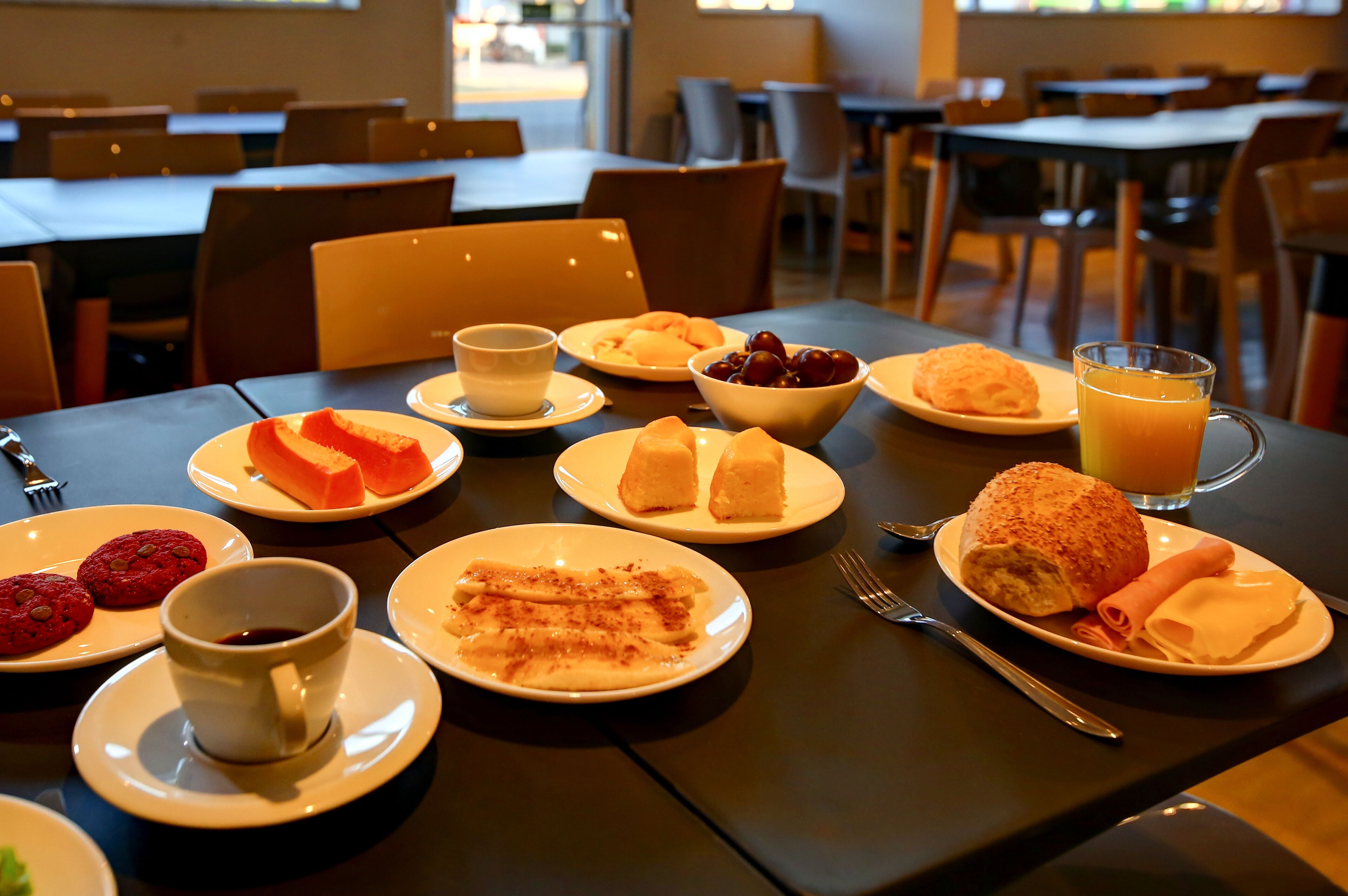 Mesa lista para el desayuno con pasteles, un vaso de jugo de naranja y una taza de café.
