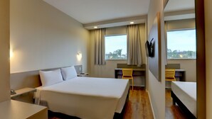 Une chambre d’hôtel avec un grand lit, un bureau avec une chaise, un téléviseur fixé au mur et une fenêtre avec des rideaux.