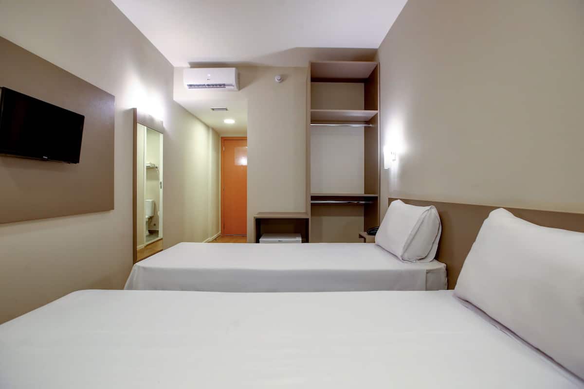 A hotel room with two beds, a TV mounted on the wall, and a walk-in closet.