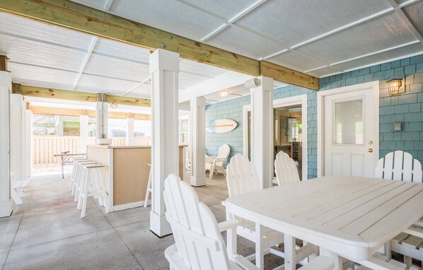 A covered outdoor dining area with white wooden furniture and a blue-tiled wall.