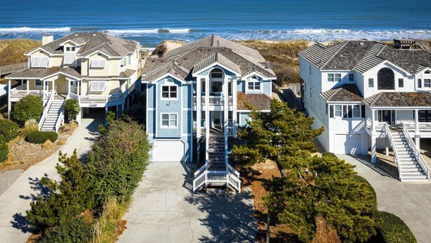 Un área residencial costera con varias casas, incluyendo una casa azul destacada con porche y una escalera que lleva a la entrada.