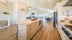 Una cocina amplia con armarios de madera, una isla grande, electrodomésticos de acero inoxidable e iluminación colgante.