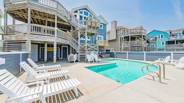 Una propiedad frente a la playa con piscina, varias terrazas y mobiliario exterior.