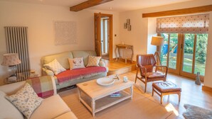 Un salon spacieux avec un plafond en bois, une grande fenêtre donnant sur un paysage verdoyant, un canapé agrémenté de coussins à motifs, une table basse et un fauteuil en cuir.