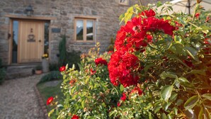 Un bâtiment en pierre doté d’une porte et de fenêtres en bois, entouré d’une abondance de fleurs rouges.