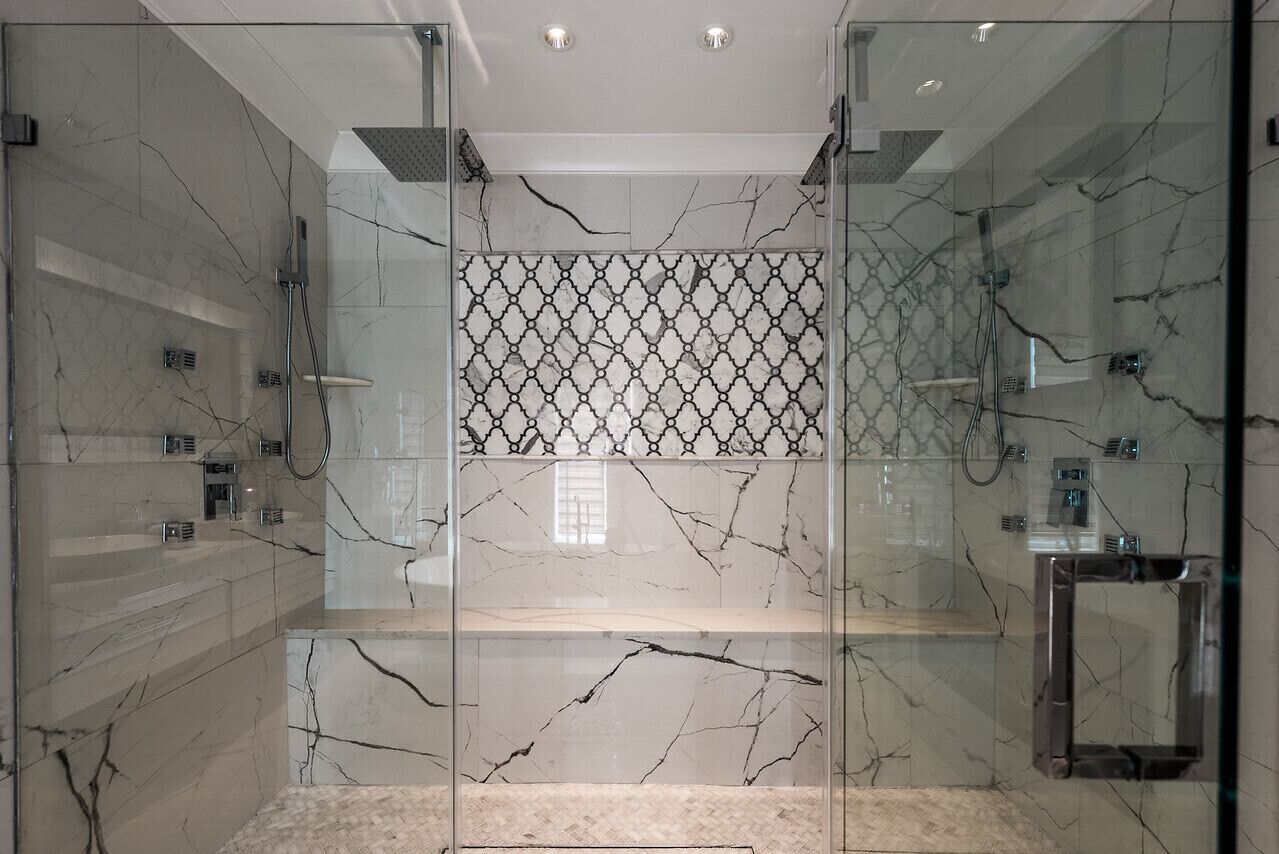Une salle de bain moderne avec des murs en marbre, une douche en verre et un motif décoratif central en mosaïque.