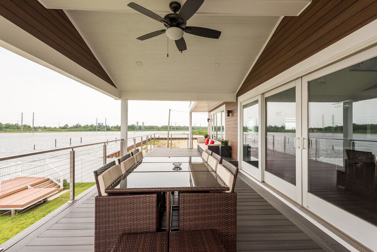 A covered outdoor deck with a table and chairs, a ceiling fan, and a view of the water.
