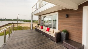 Terraza moderna al aire libre con un sofá y cojines, con vista a un cuerpo de agua y un paisaje distante.