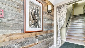 Pared de madeira com um quadro emoldurado, luminária fixada na parede e escada com cortinas estampadas.