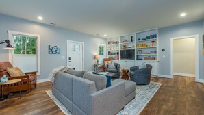 Una sala de estar con un sofá gris, una mesa de centro de madera y una estantería llena de libros y objetos decorativos.