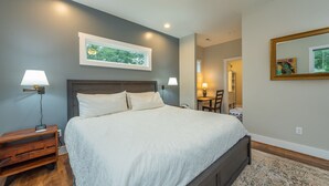 Un dormitorio con una cama grande, dos lámparas de noche, una mesita de noche, un escritorio con una silla, un espejo y un cuadro en la pared.