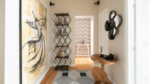 Un couloir orné d’un grand tableau abstrait, d’un tapis à motifs géométriques, d’une table en bois sur laquelle est posé un vase, et d’une bibliothèque remplie de livres et d’objets décoratifs.