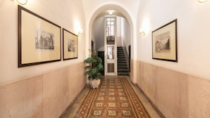 Un couloir avec des tableaux encadrés accrochés aux murs, un sol à motifs et un escalier en arrière-plan.