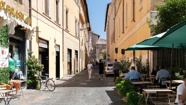 Une ruelle étroite pavée, bordée d’immeubles, d’espaces aménagés pour les terrasses et d’un vélo garé devant une boutique.