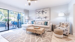 A modern living room with a large window, a ceiling fan, a sofa, a coffee table, and a patterned rug. - Golf Cart ~ Lake Views ~ Community Pool ~ Patio (Miramar Beach)