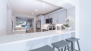 A modern kitchen with white cabinetry, a stainless steel refrigerator, a microwave, and a large island with bar stools. - Golf Cart ~ Lake Views ~ Community Pool ~ Patio (Miramar Beach)